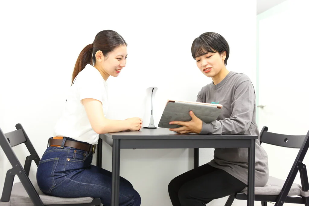 テーブルでタブレットを見ながら女性に説明するスタッフ