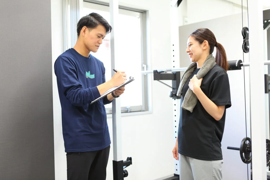バインダーに記入しながら女性と話すトレーナー