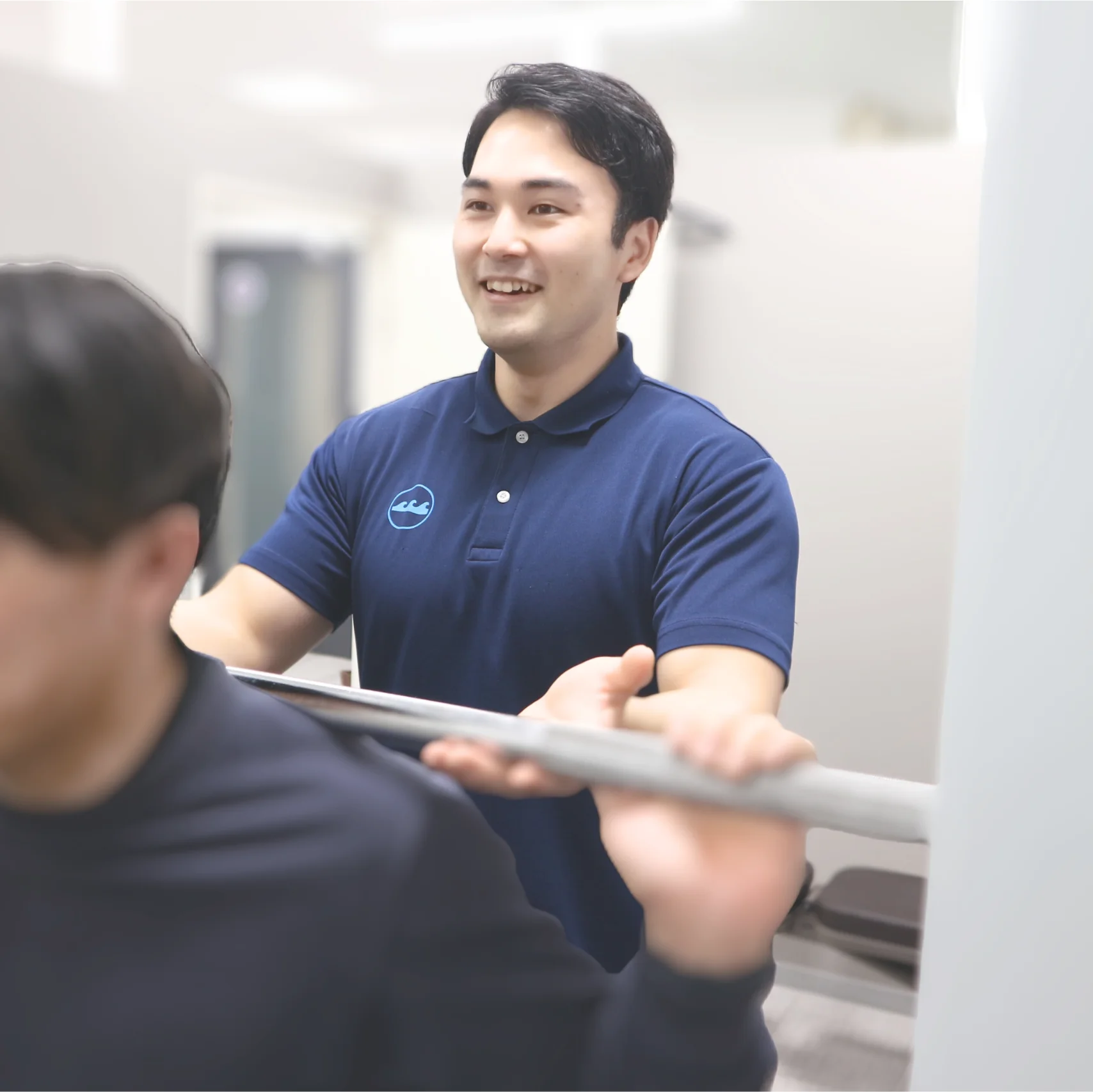 バーベルを担ぐ男性の横で笑顔でサポートするトレーナー