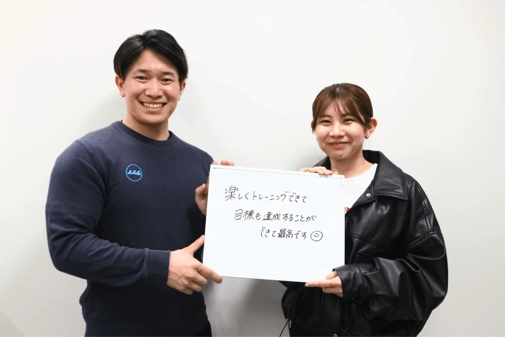 「目標も達成することができて最高です」と書いたボードを持つトレーナーと女性会員